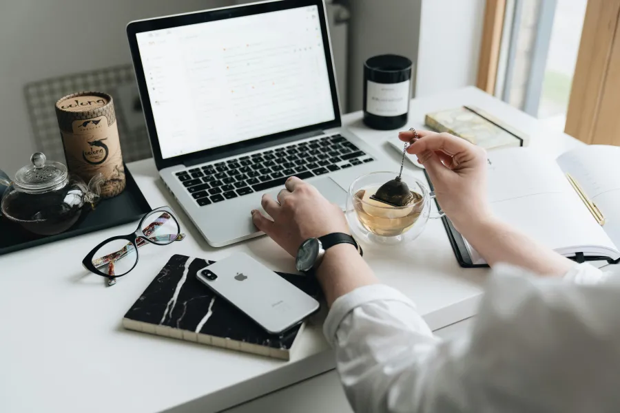 person at their desk with a laptop and pot of tea